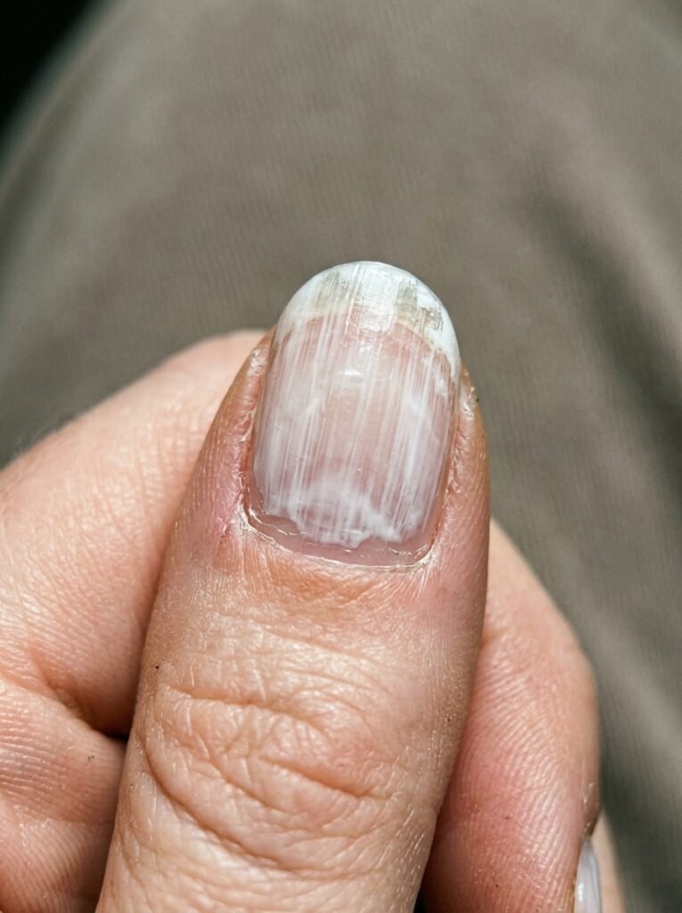 Close-up of streaky milky white polish showing brush marks and a thin tip