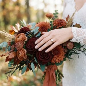 Bride's hand with a minimalist warm nude manicure resting on a fall bouquet